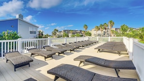 Um terraço com espreguiçadeiras e cerca branca, com vista para a praia e edifícios.