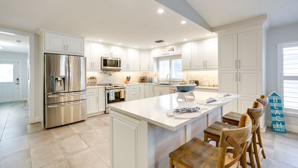 Una cocina moderna con armarios blancos, electrodomésticos de acero inoxidable y una isla central con taburetes de bar.