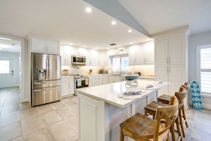 A modern kitchen with white cabinetry, stainless steel appliances, and a central island with bar stools.