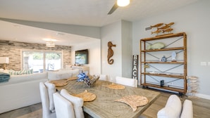 Un salón moderno con una gran mesa de comedor de madera, sofás blancos y una estantería decorativa con peces.