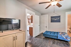 A room with a TV on a wooden cabinet, a blue sofa, a ceiling fan, and a wall with a moon phase decoration. - Cozy Galveston Apartment - Walk to Beach & Dining (Galveston)