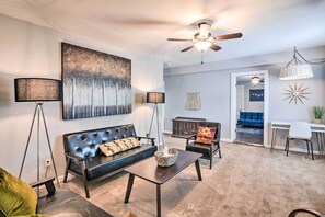 A modern living room with a black sofa, a coffee table, and a ceiling fan. - Cozy Galveston Apartment - Walk to Beach & Dining (Galveston)