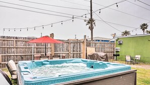 Ein Whirlpool mit Holzterrasse, einem roten Sonnenschirm und einem Holzzaun im Hintergrund.