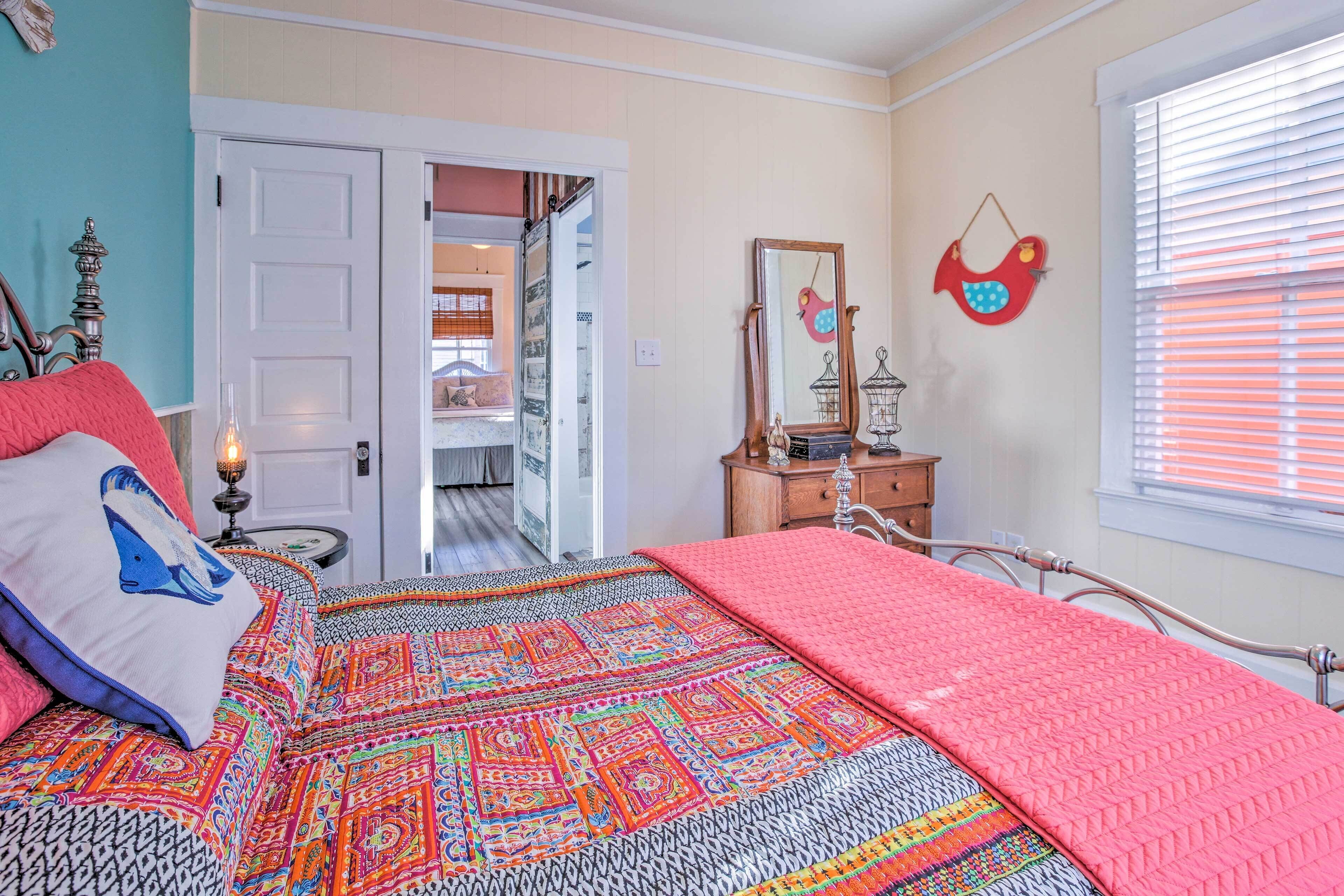 A bedroom with a bed, a bedside table with a lamp, a dresser, a mirror, and a window with blinds.