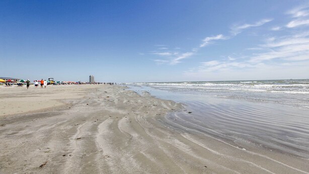 Una spiaggia con una battigia sabbiosa e alcune persone che passeggiano.
