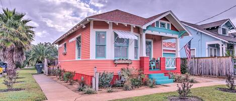 A two-story house with a red exterior and blue trim, a front porch with steps, and a small front yard with landscaping.