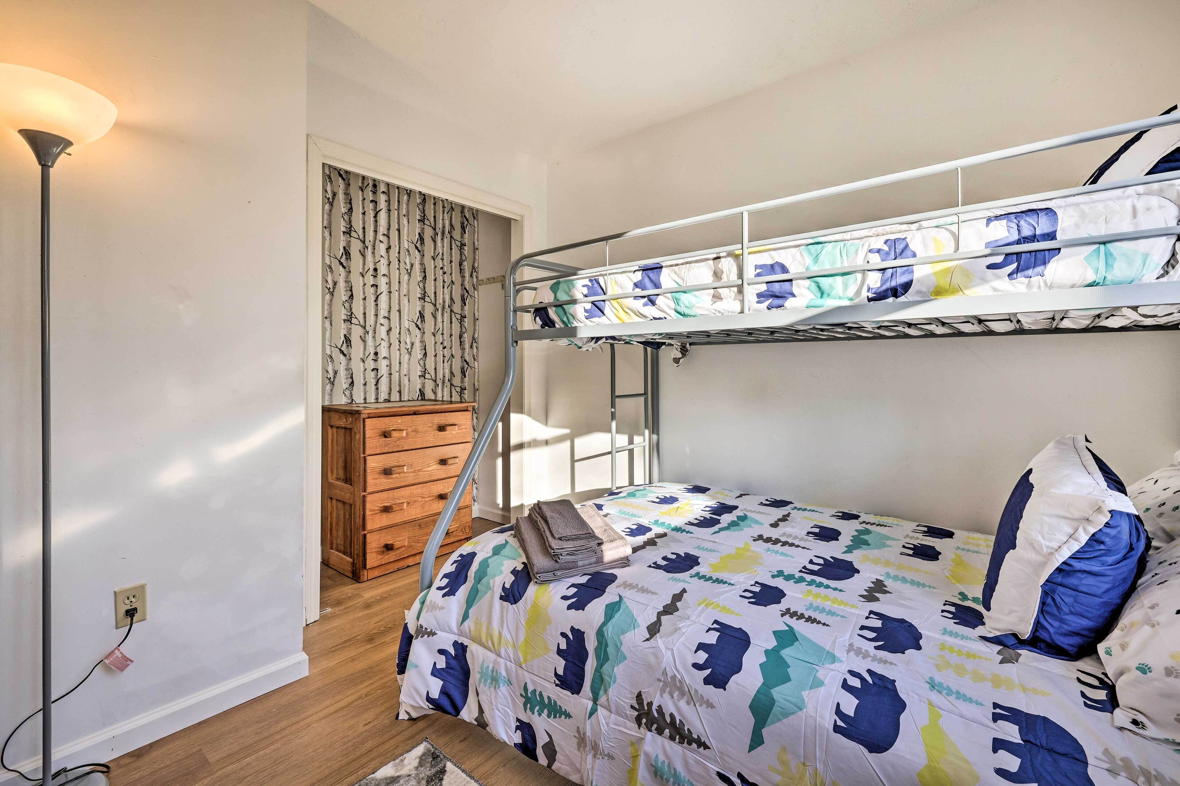 A bunk bed with a colorful quilt, a wooden dresser, a floor lamp, and a window with curtains.