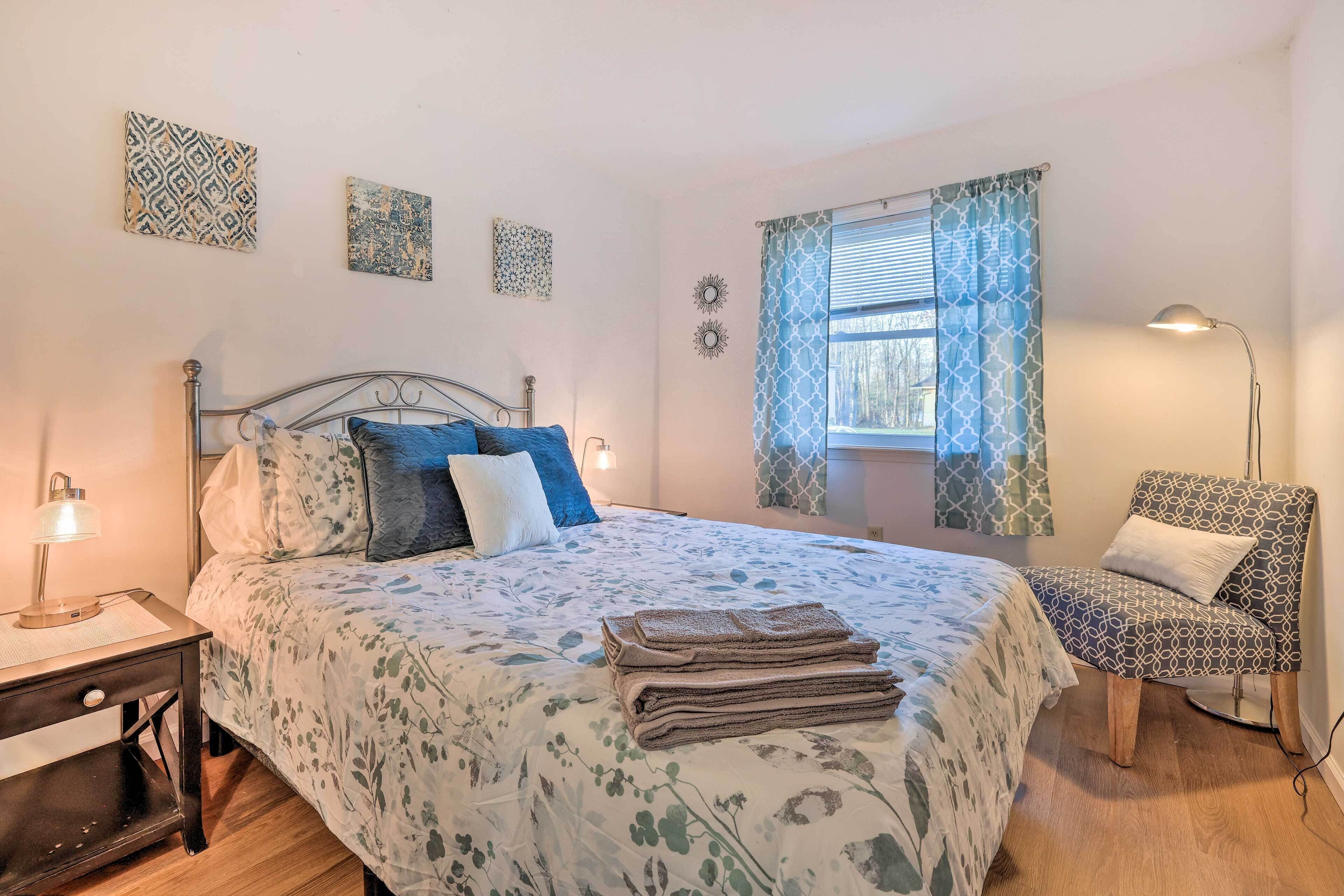 A bedroom with a bed, bedside tables, a chair, and a window with patterned curtains.