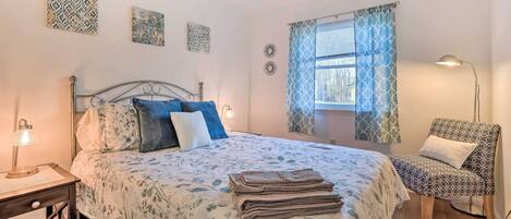 A bedroom with a bed, bedside tables, a chair, and a window with patterned curtains.