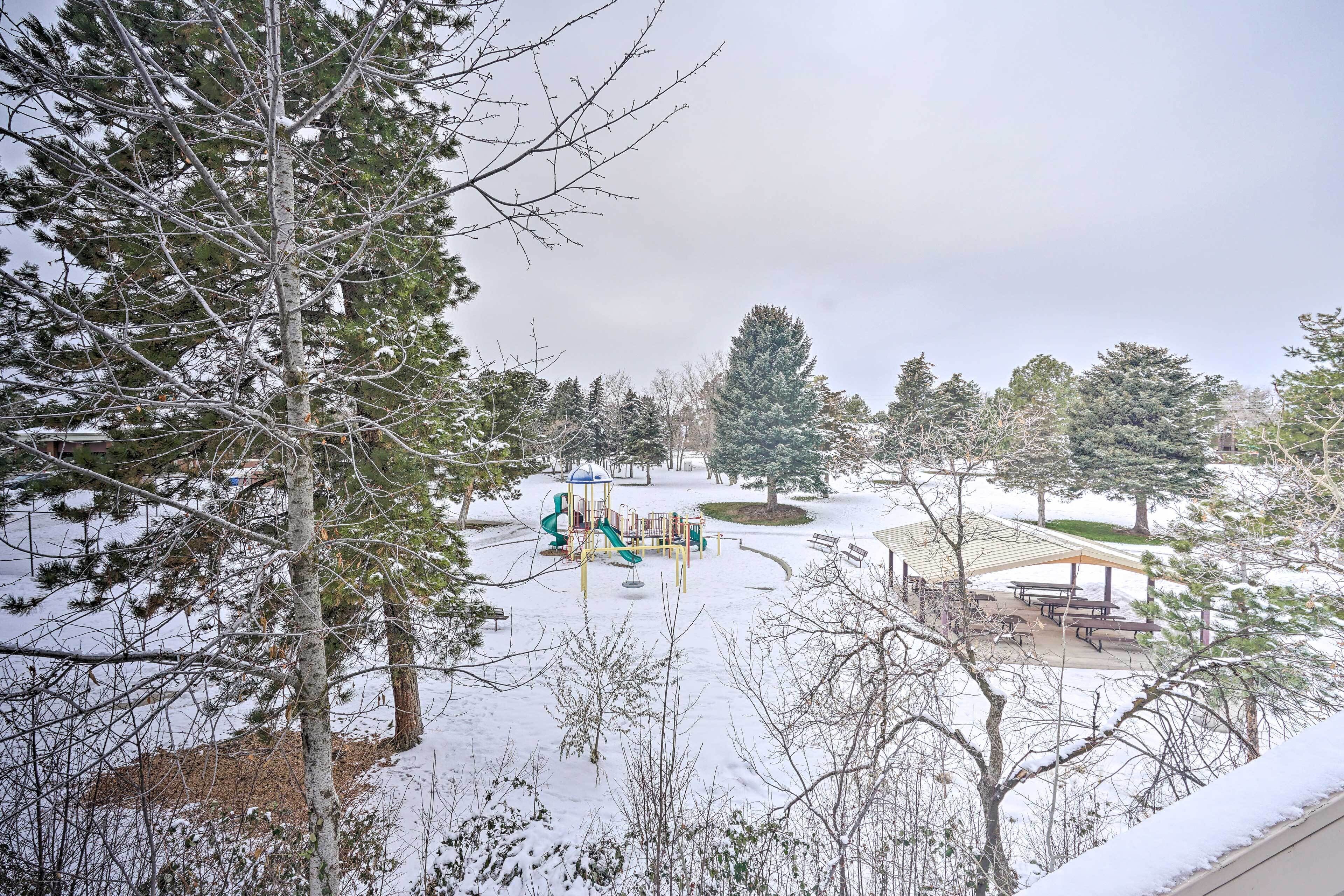 A snow-covered park with playground equipment and picnic tables.
