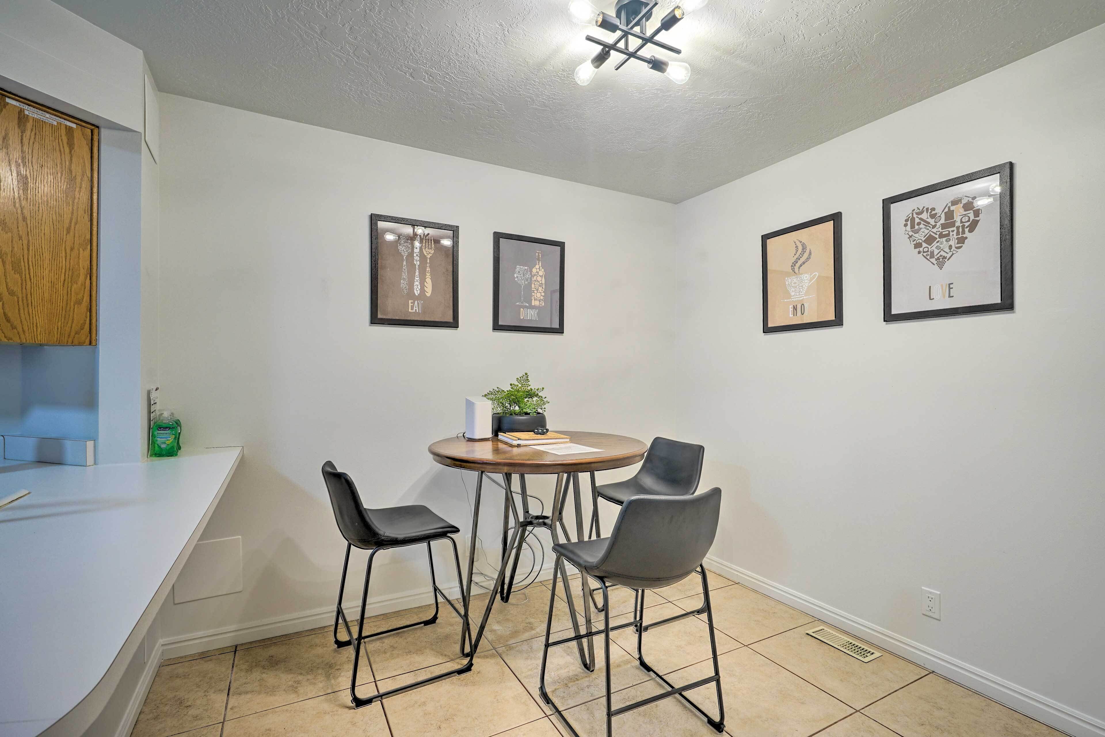 A small dining area with a round table and two chairs, a wooden cabinet, and three framed pictures on the wall.