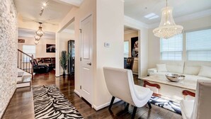 A spacious living room with a white sofa, a coffee table, and a chandelier. There is a staircase leading to another level, and a zebra-patterned rug on the floor. - Downtown DC Home w/ Furnished Patio! (Washington)