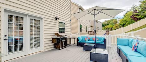 Een overdekt terras met tuinmeubilair, een barbecue en een grote parasol.