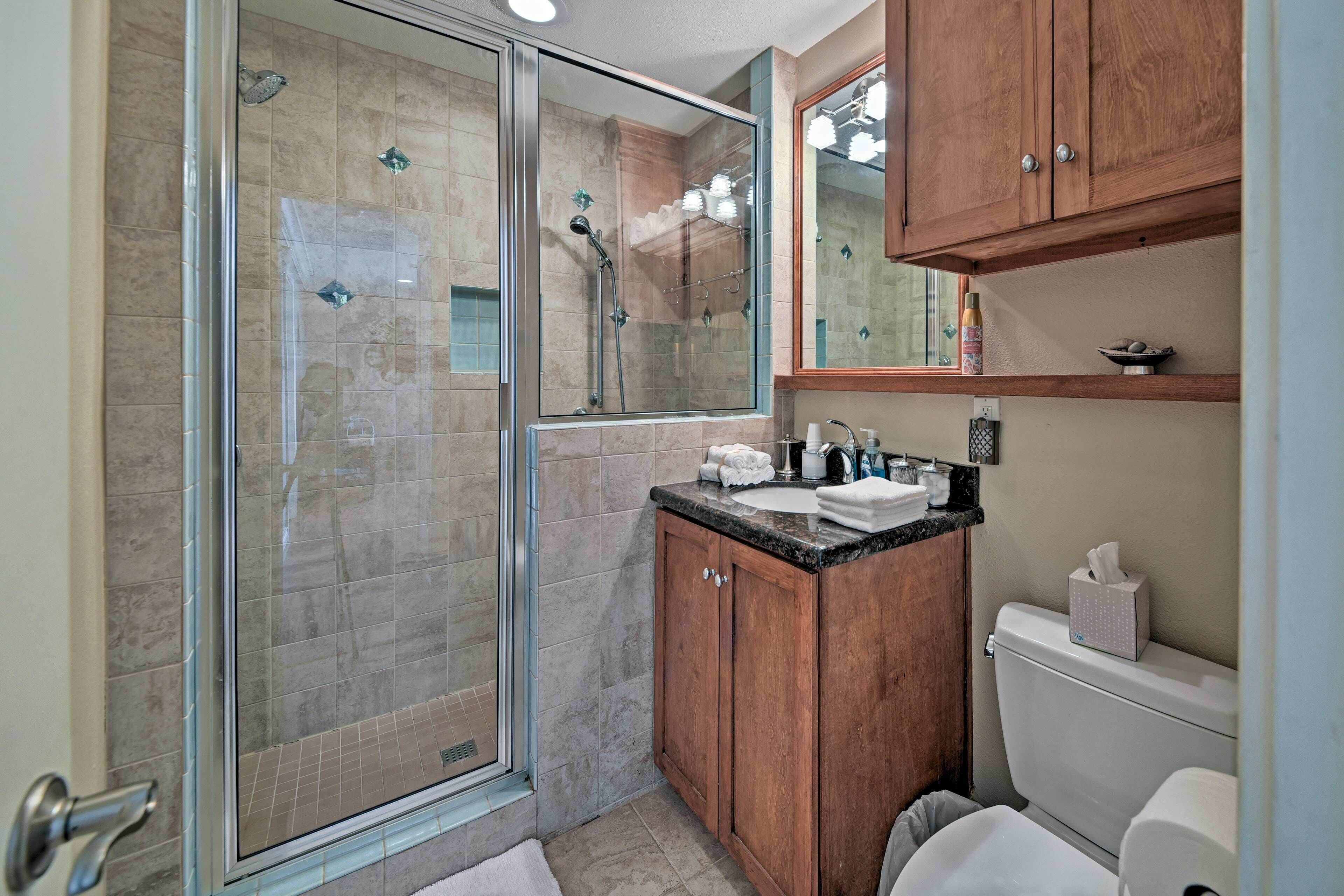 A modern bathroom with a glass-enclosed shower, wooden cabinets, a sink with a countertop, and a toilet.
