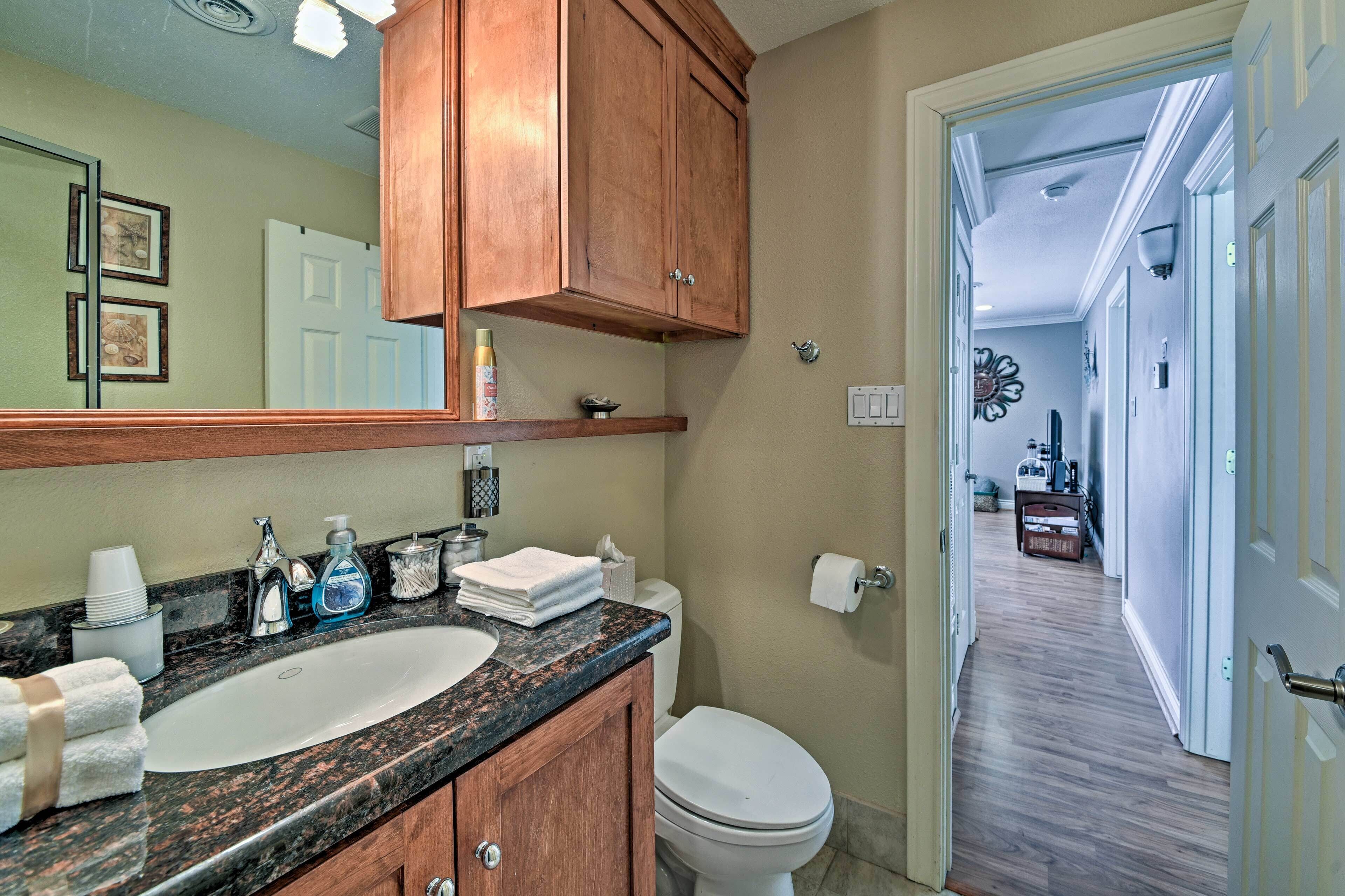 A bathroom with a granite countertop, a white sink, wooden cabinets, and a toilet.