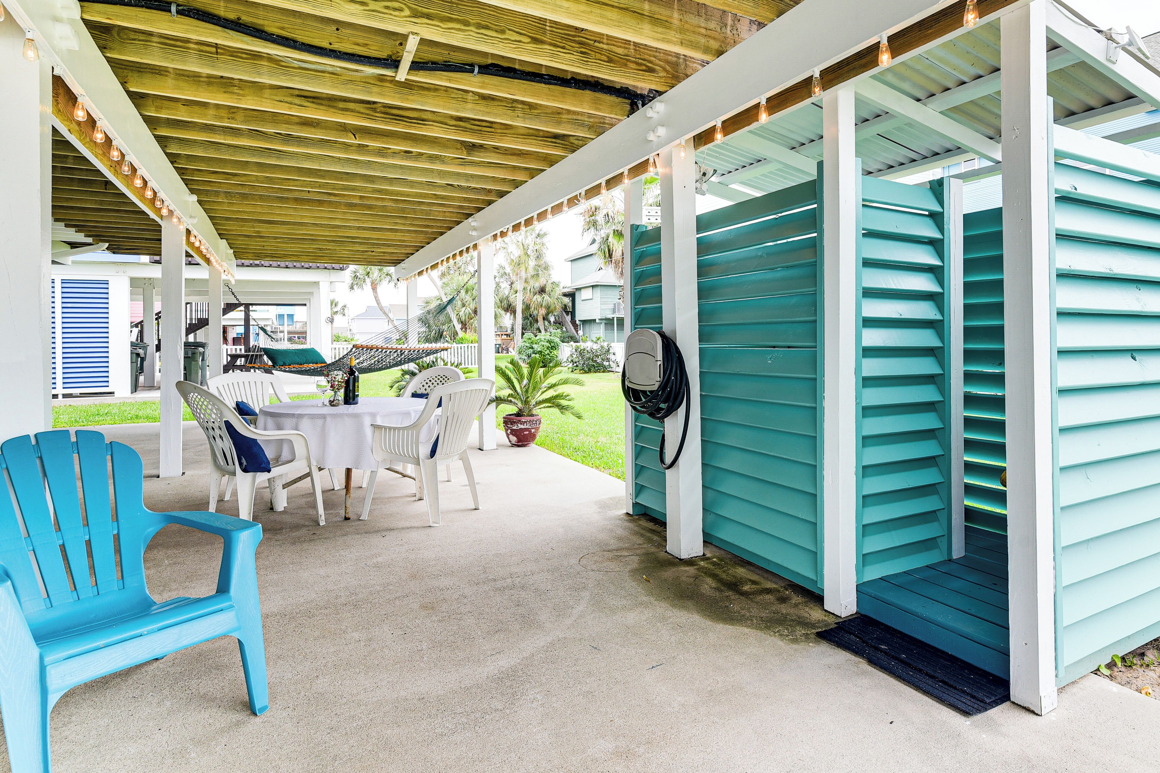 Un'area patio coperta con tavolo e sedie, una sedia blu e un edificio color verde acqua con una porta.