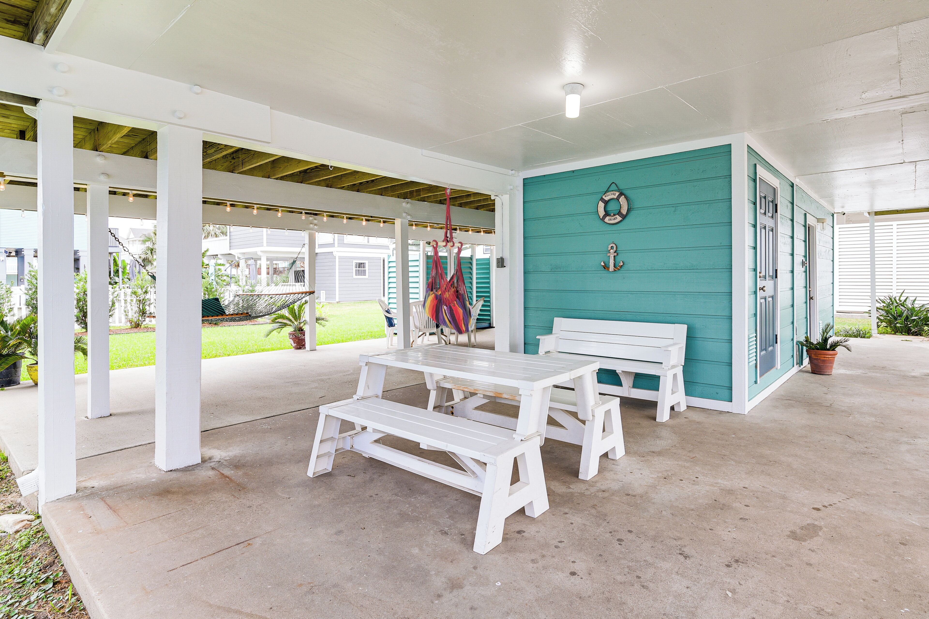 A covered patio with a white table and bench, turquoise walls, and a hanging hammock.