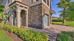A two-story house with a stone facade, a green door, and a paved driveway. - Luxe Reunion House w/ Private Pool: Near Disney! (Kissimmee)