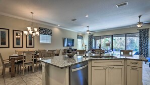 A modern kitchen with a central island, built-in appliances, and a dining area with wooden chairs and a chandelier. - Luxe Reunion House w/ Private Pool: Near Disney! (Kissimmee)