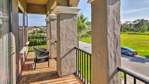 A balcony with a view of a road and greenery, featuring a wicker chair and a small table. - Luxe Reunion House w/ Private Pool: Near Disney! (Kissimmee)