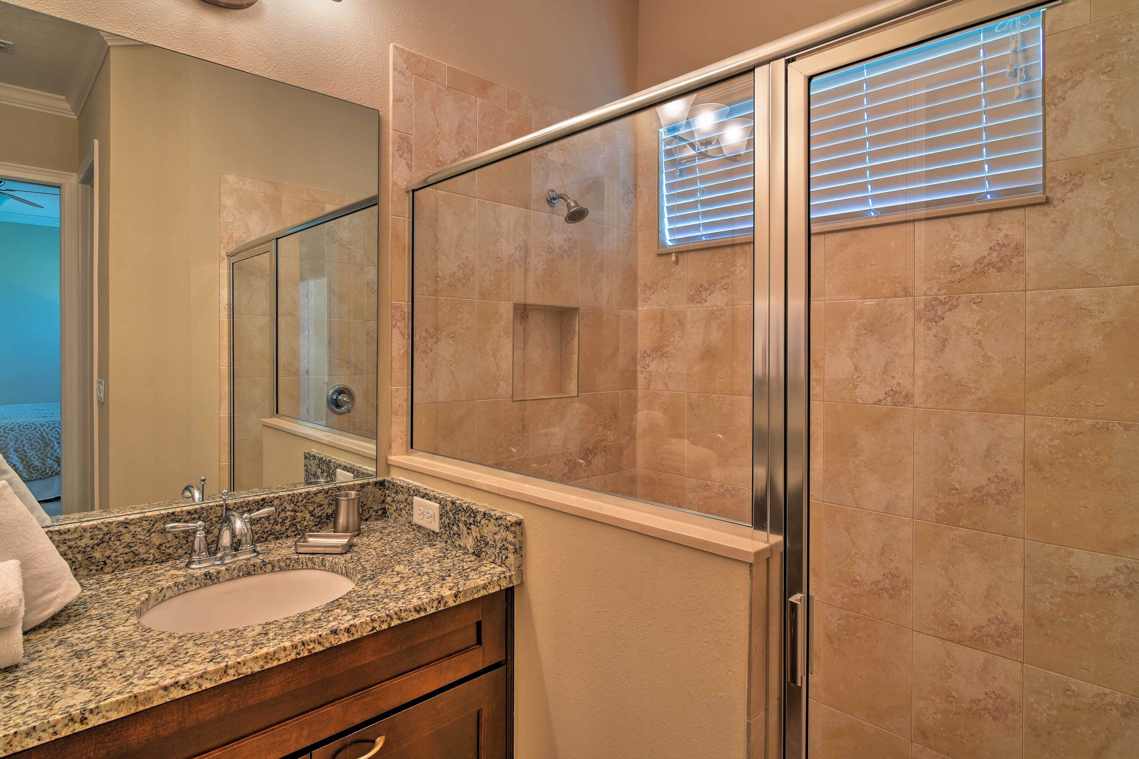 A bathroom with a glass-enclosed shower, a sink with a granite countertop, and a mirror above the sink.
