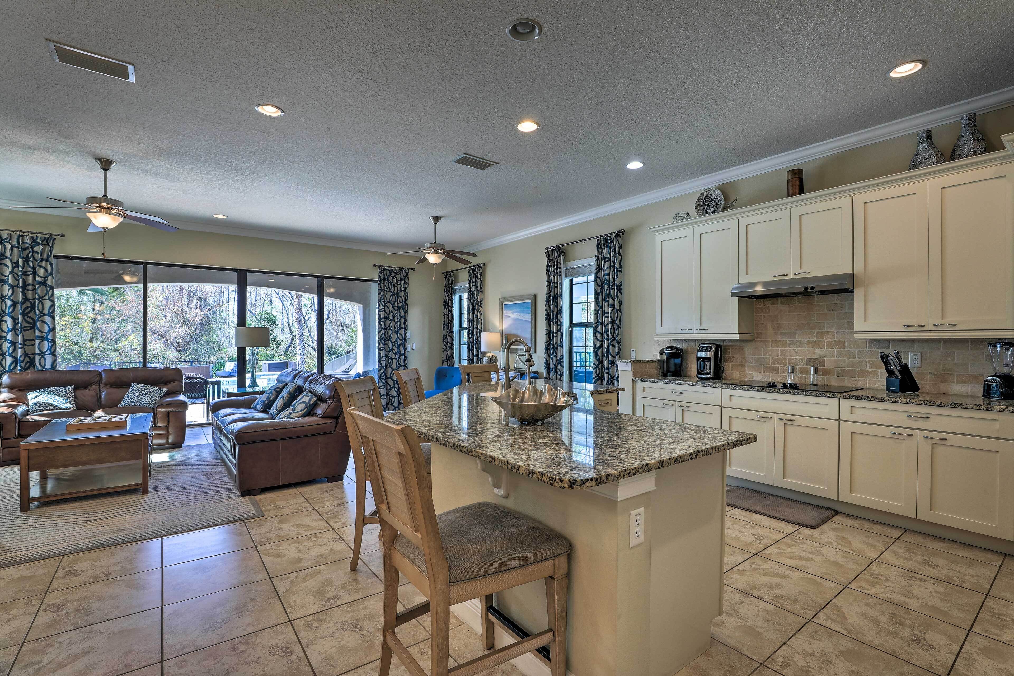 A spacious living area with a large island, a kitchen with white cabinets, and a dining area with a brown leather couch.