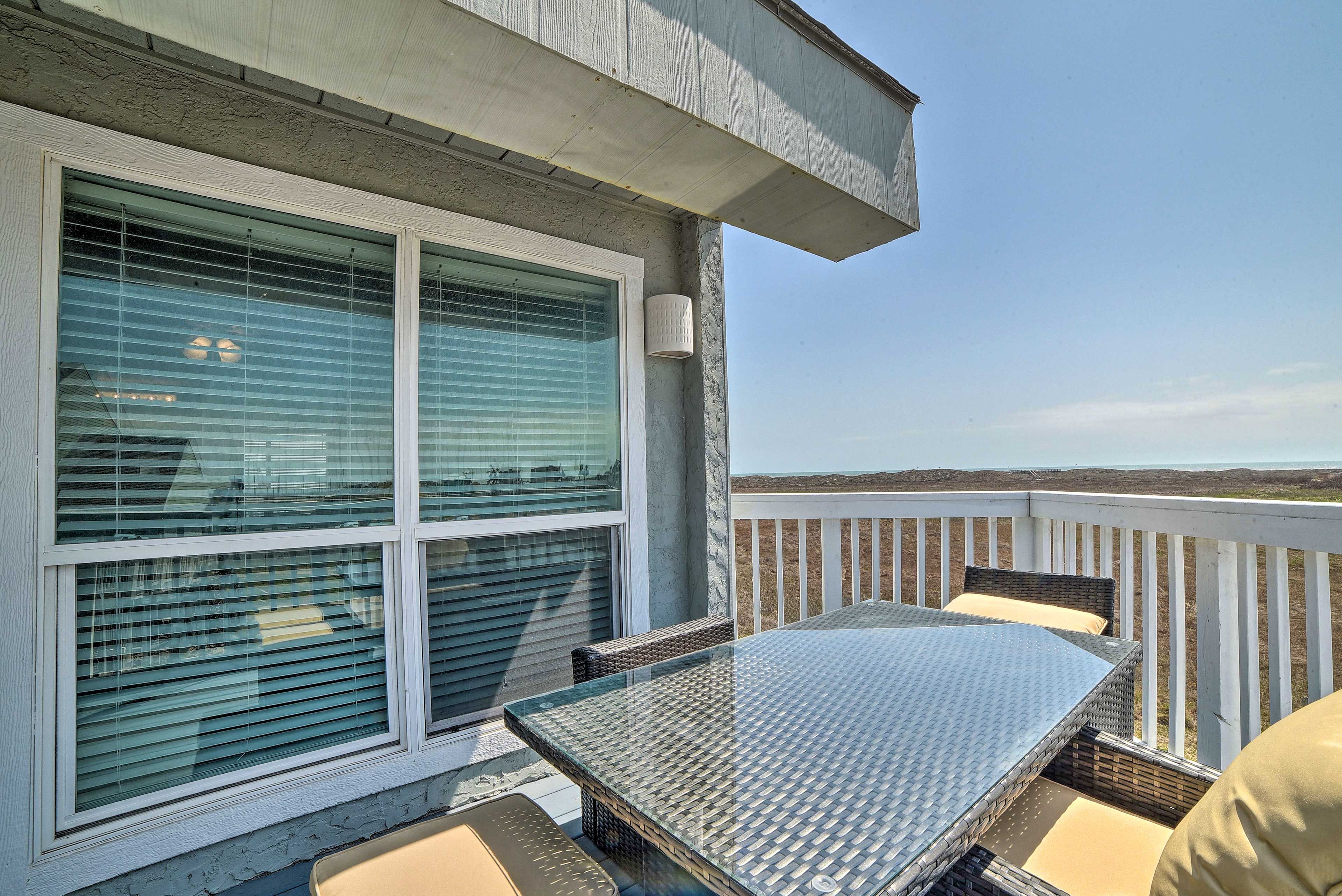 Un balcon avec une table et des chaises en verre, une balustrade blanche et une vue sur le paysage.