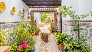 Ein schmales Innenhof mit Fliesenwänden, Topfpflanzen und einer Holzpergola.