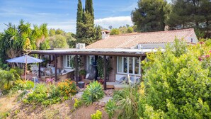 Ein Haus mit überdachter Terrasse, Gartenmöbeln und einem Garten mit verschiedenen Pflanzen und Blumen.