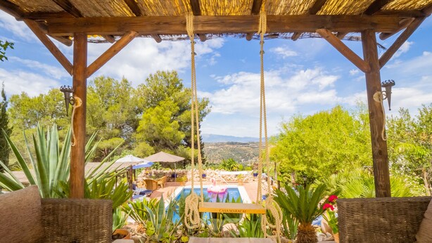 Eine hölzerne Pergola mit einer Schaukel, Sitzgelegenheiten im Freien und Blick auf einen Pool und die Landschaft.