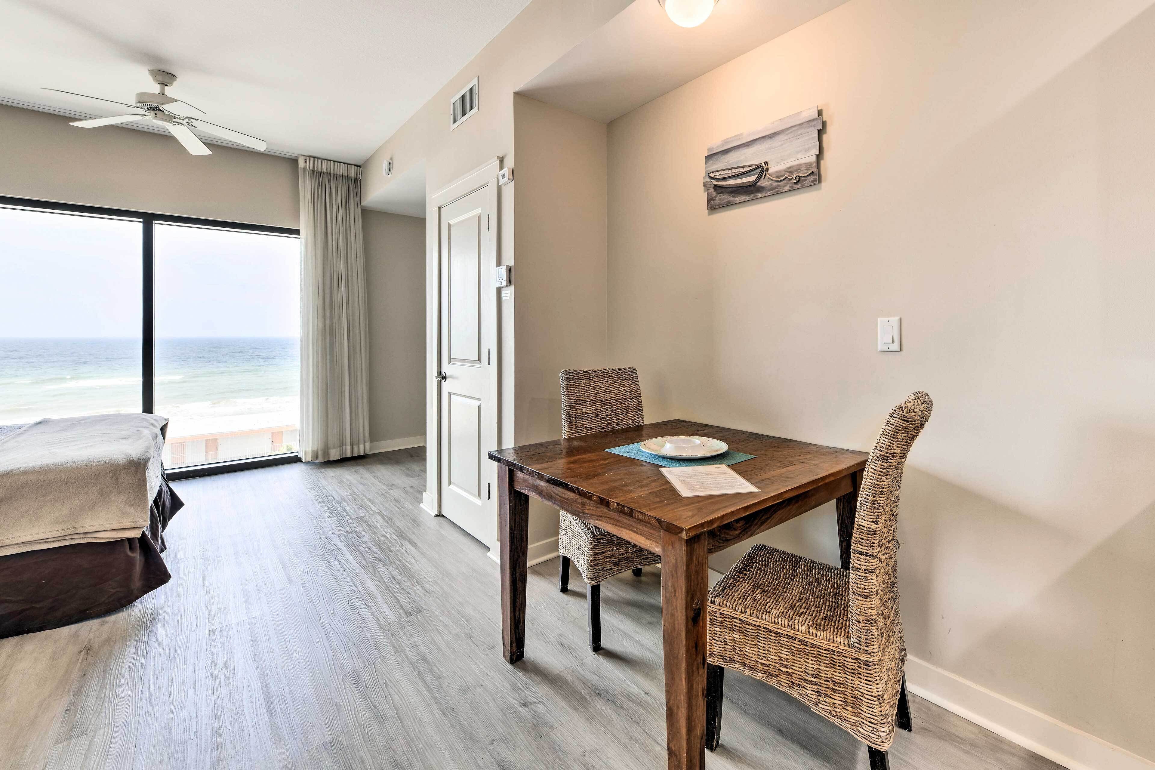 A hotel room with a dining area, a bed, a view of the ocean, and a ceiling fan.