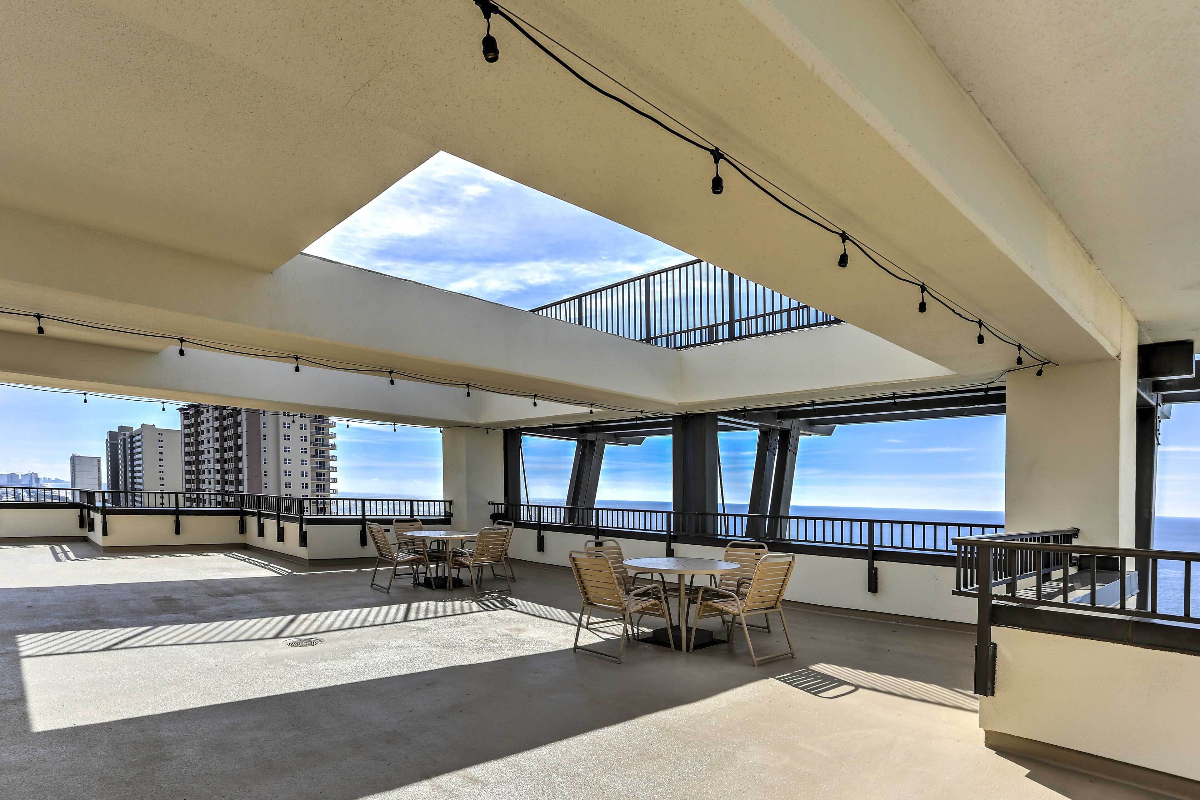 A spacious rooftop terrace with multiple tables and chairs, large windows offering ocean views, and a skylight.
