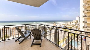 Un balcon avec vue sur l’océan et la plage, une piscine et un fauteuil.