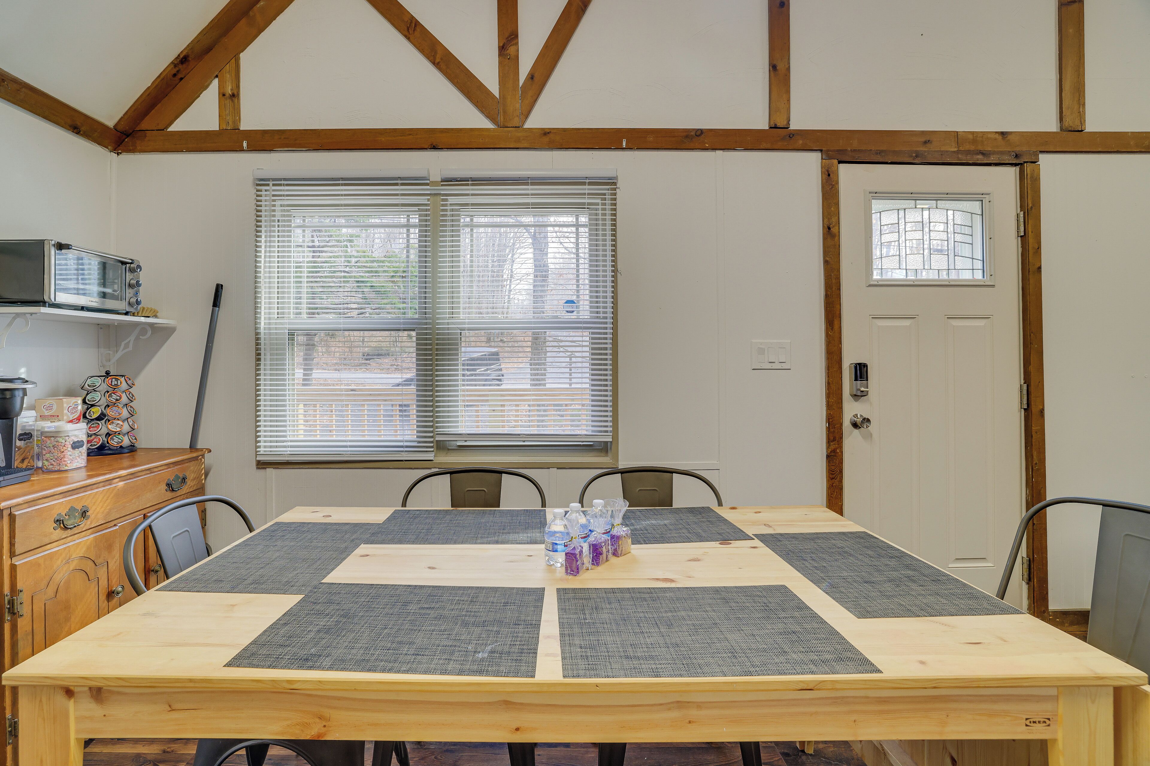 A dining area with a wooden table, four chairs, a microwave, and a window with blinds.