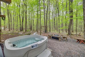 A hot tub in a forested area with picnic tables and a wooden bench. - Hot Tub & Resort Amenities: Pocono Lake Retreat! (Pocono Lake)