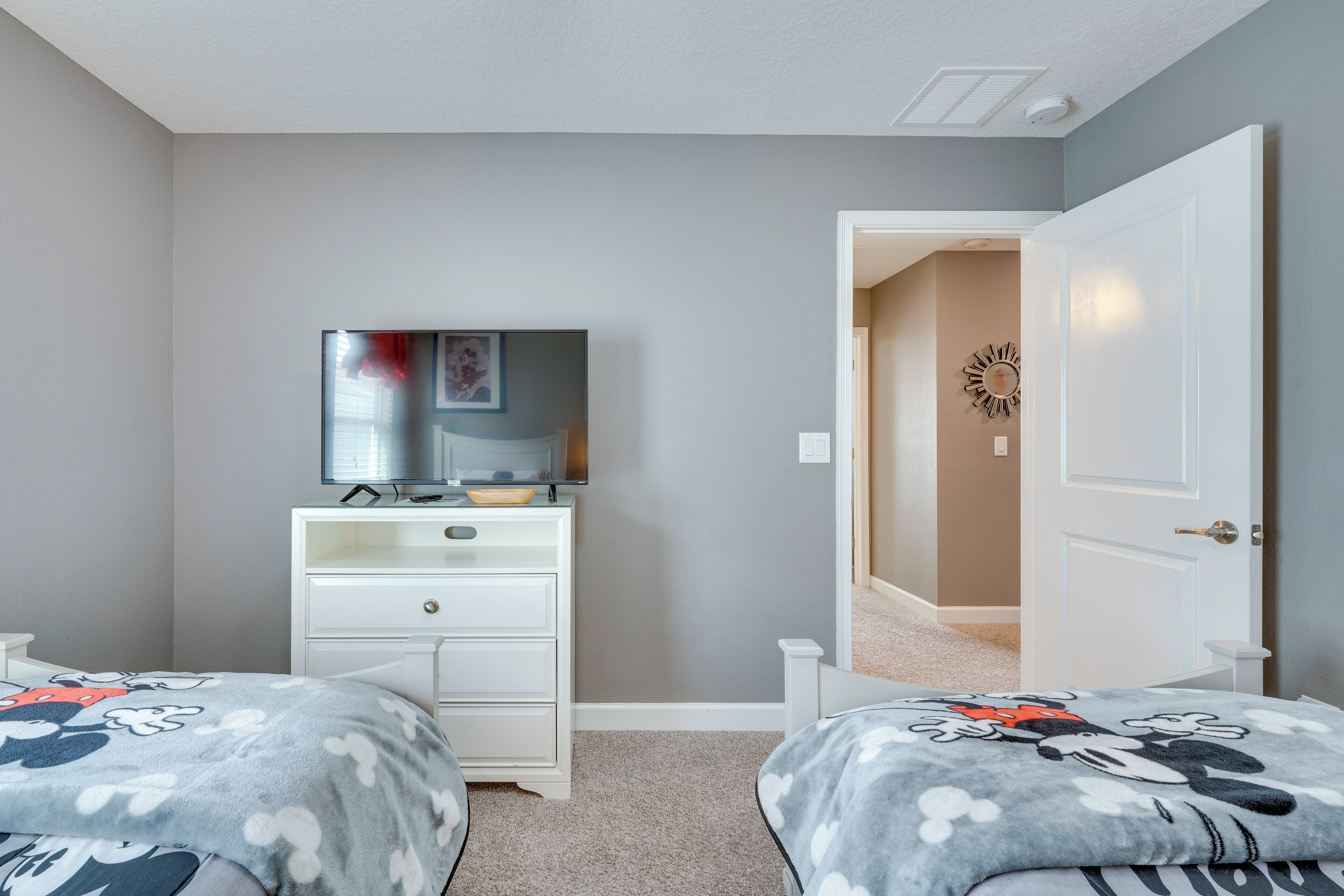 Une chambre avec deux lits, une commode, un téléviseur et une porte donnant sur une autre pièce.