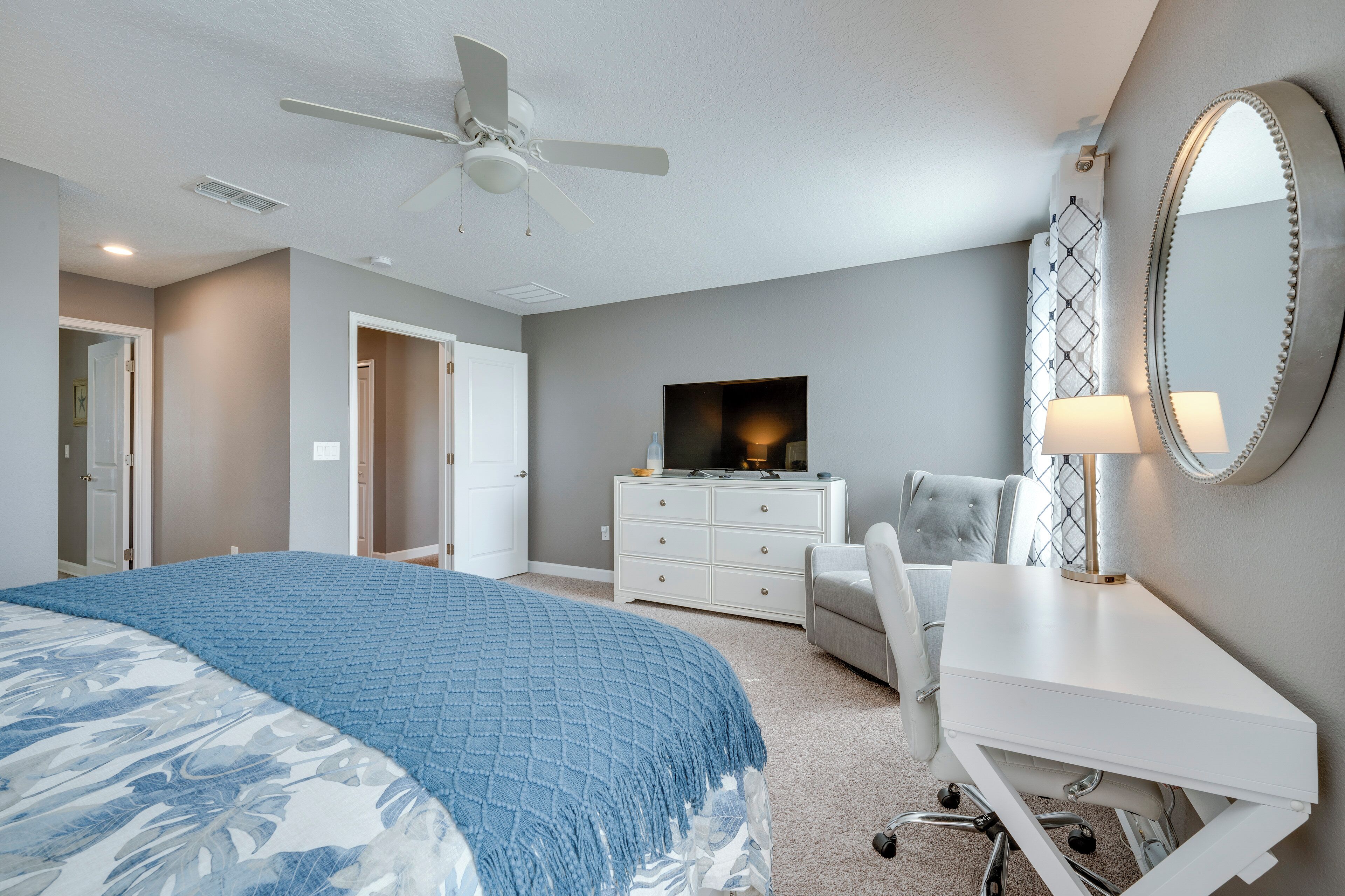 A bedroom with a bed, a desk, a chair, a TV, and a ceiling fan.