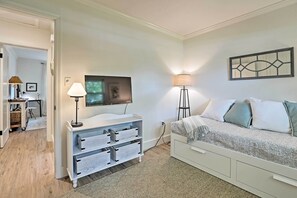Quarto moderno com uma cama, uma TV, um abajur e uma cômoda branca com gavetas.
