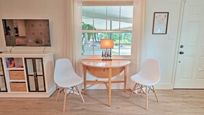 A room with a wooden table, two white chairs, a TV on a cabinet, and a window with a view of greenery. - Orlando Vacation Rental < 2 Miles to Lake Ivanhoe! (Orlando)