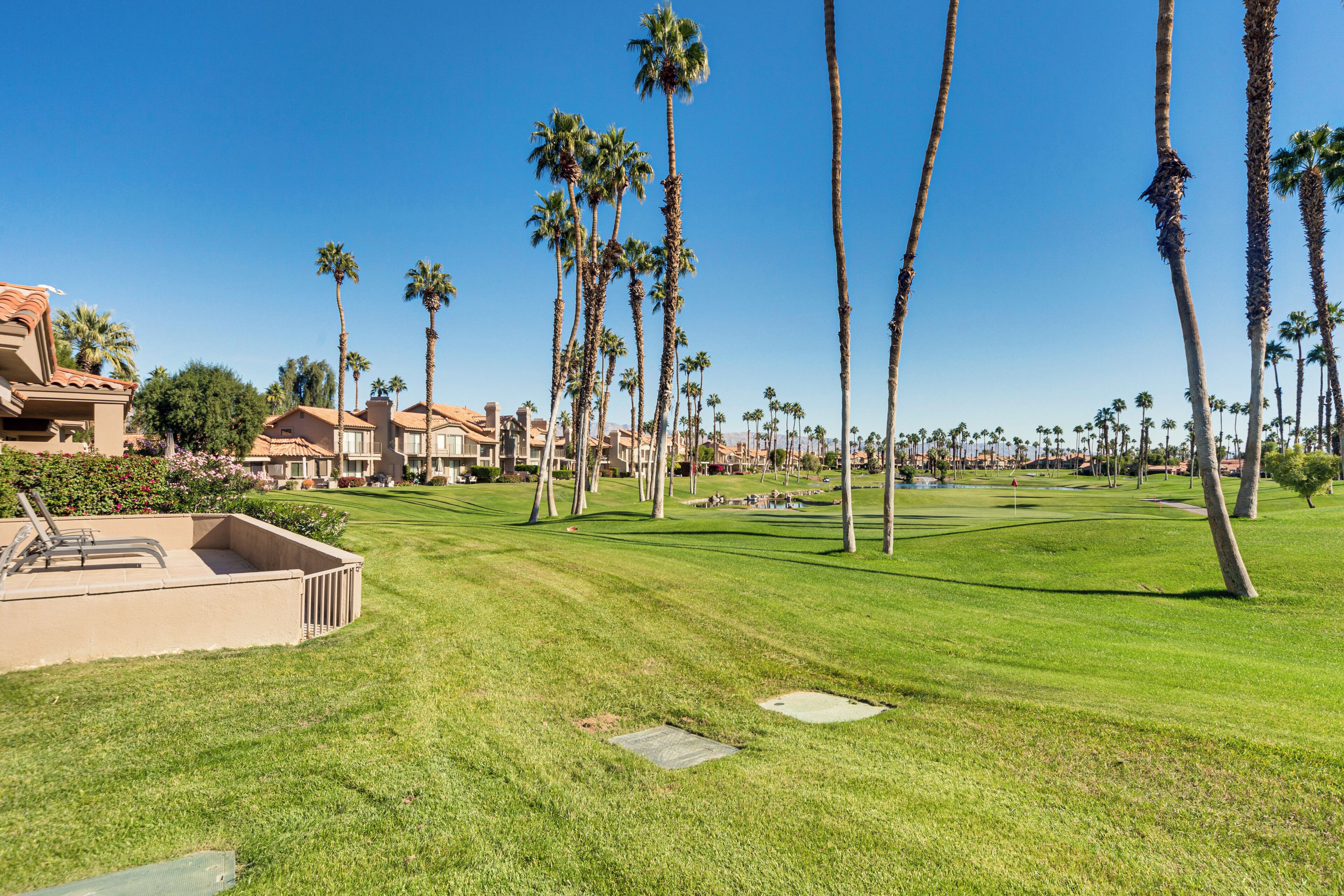 A well-maintained golf course with neatly trimmed grass, palm trees, and a clear blue sky.
