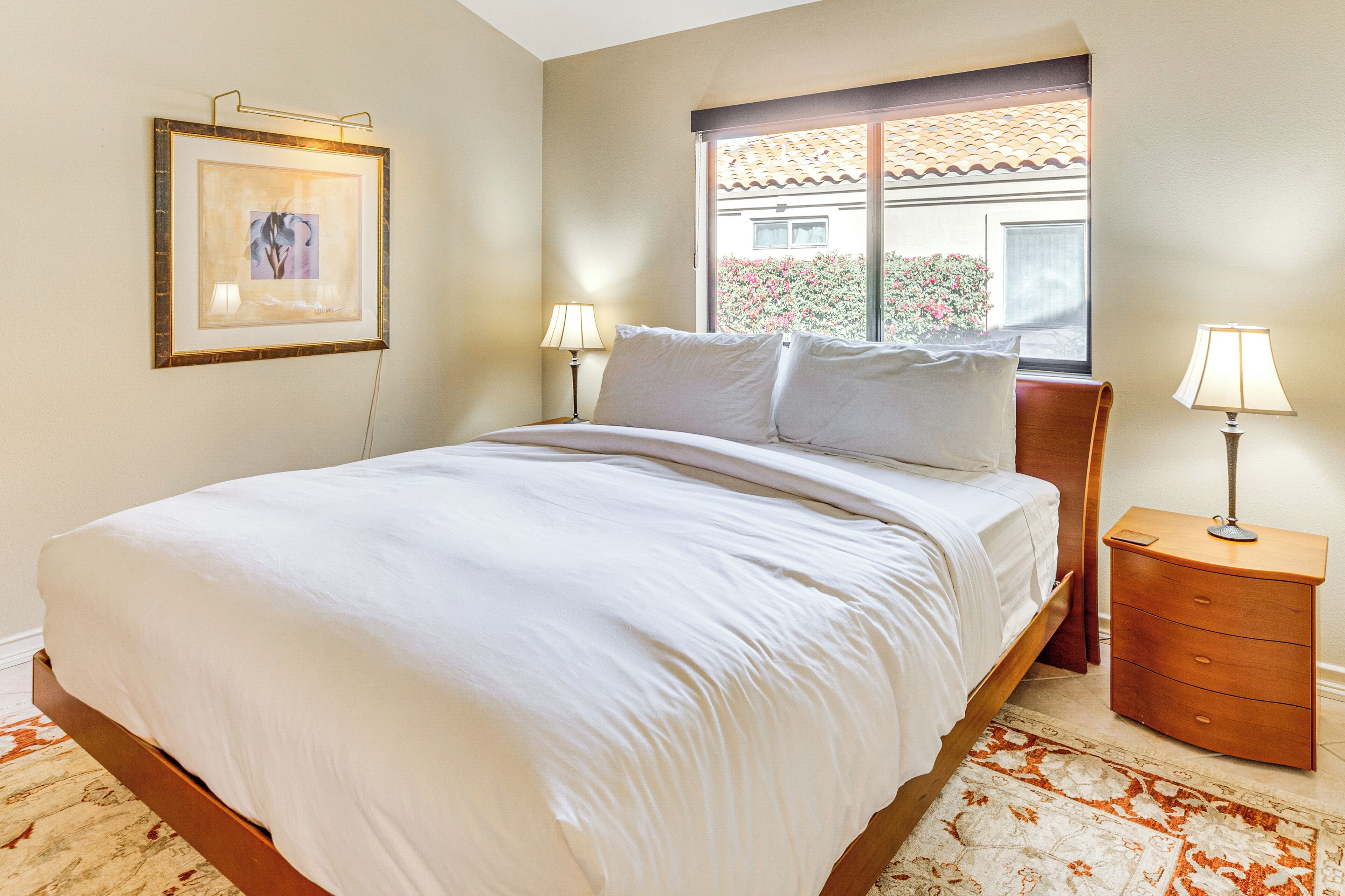 A neatly made bed with white linens, a bedside table with a lamp, and a framed picture on the wall.