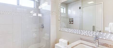 A modern bathroom with a glass-enclosed shower, a large mirror, and a sink with a granite countertop.