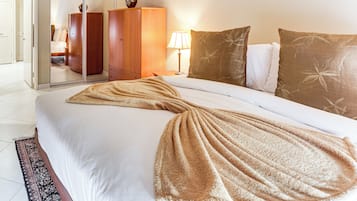 Una cama bien tendida con una manta color beige, un armario de madera y una lámpara de noche en una habitación de hotel.