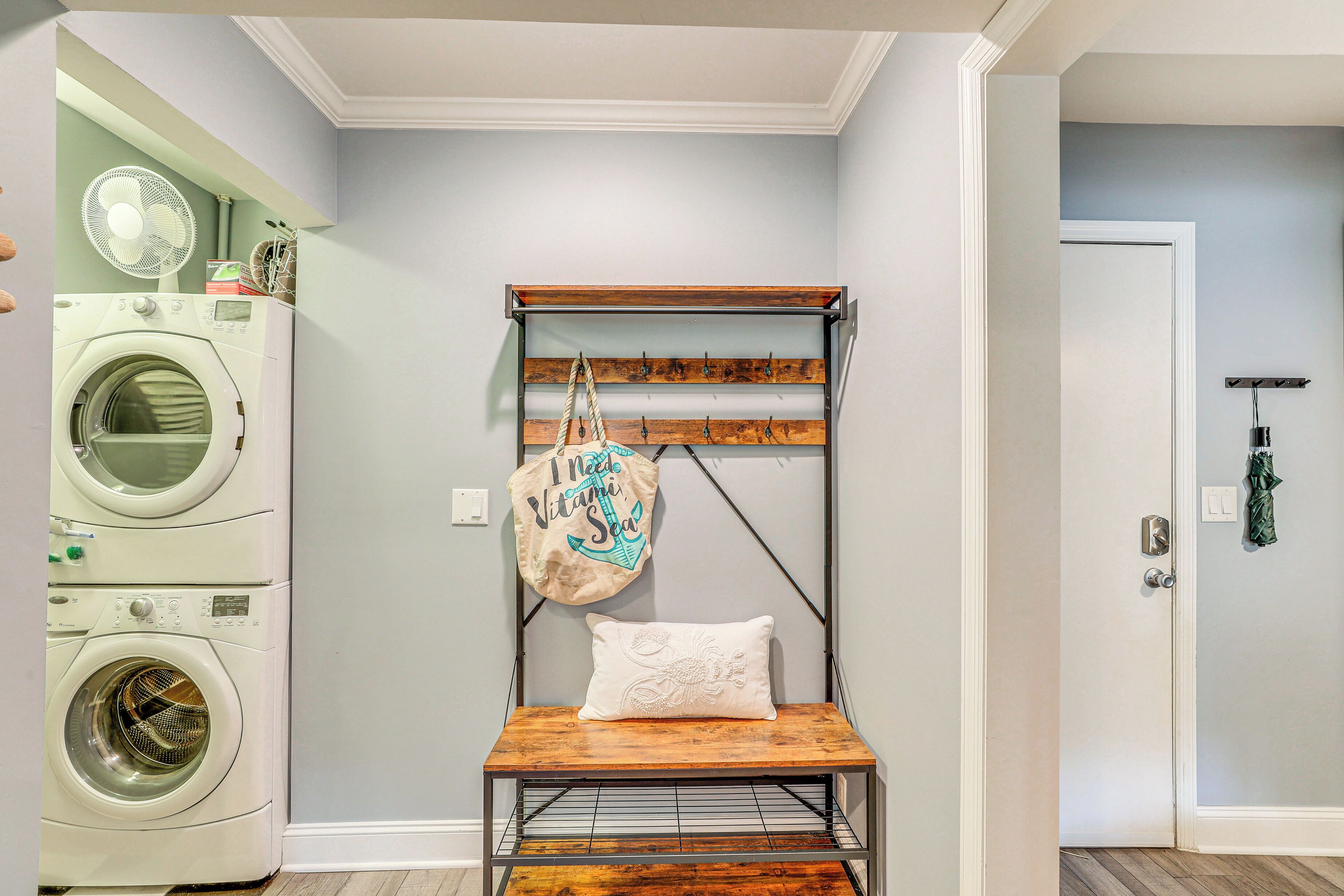A laundry room with stacked washers and dryers, a wooden bench with a pillow, and a wall-mounted rack with hooks.