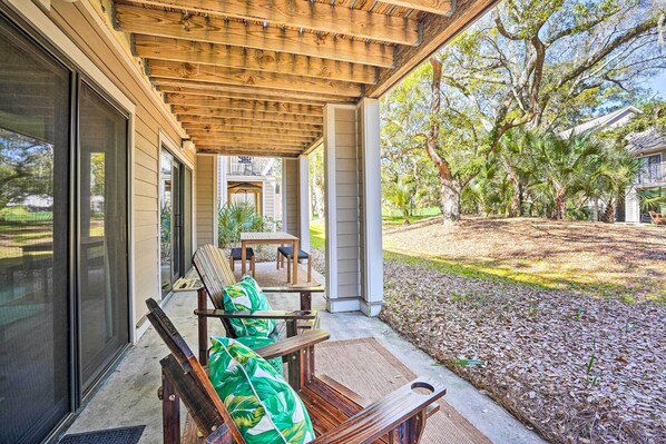 A covered patio with outdoor furniture, a view of a house, and a landscaped yard.
