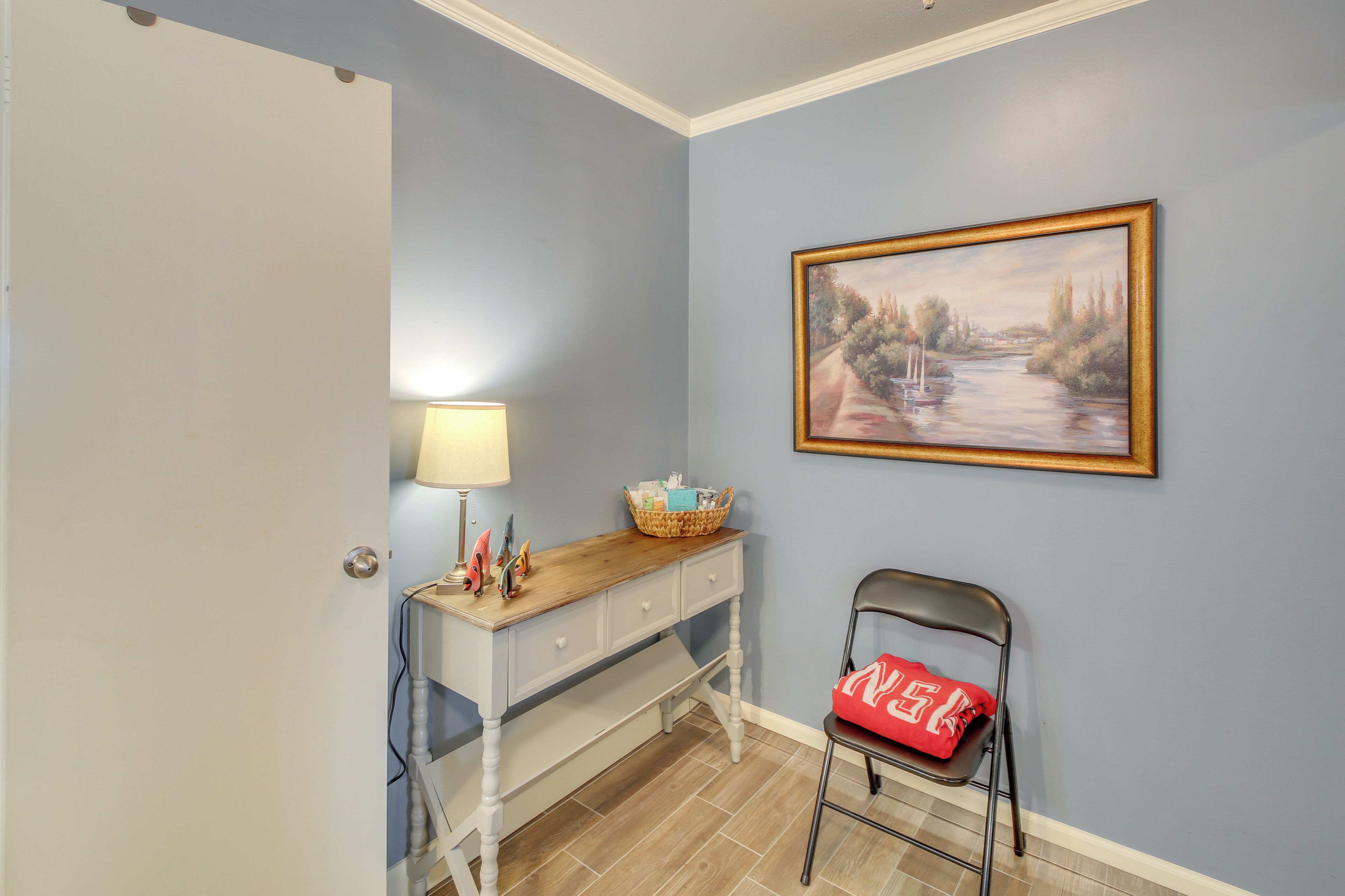 A room with a desk, chair, lamp, and a painting on the wall.