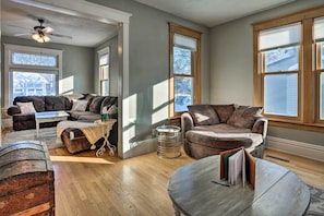 A spacious living room with a large window, a ceiling fan, and a cozy seating area with multiple couches and a coffee table. - Saint Paul Home in Historic Cathedral Hill (St. Paul)