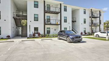 A multi-story residential building with a central staircase, balconies, and a parking area with two cars.