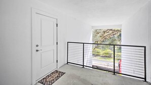 A white door with a metal gate, a concrete floor, and a view of greenery outside.