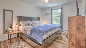 A bedroom with a bed, a ceiling fan, a nightstand, a lamp, a dresser, and a window with curtains.